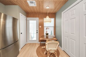 A modern kitchen with a stainless steel refrigerator, a wooden dining table with chairs, and a hanging light fixture.
