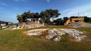 A stone structure with a thatched roof, surrounded by grass and trees, under a clear sky.