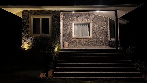 A modern house with stone walls, a set of stairs leading to a door, and two windows with curtains.
