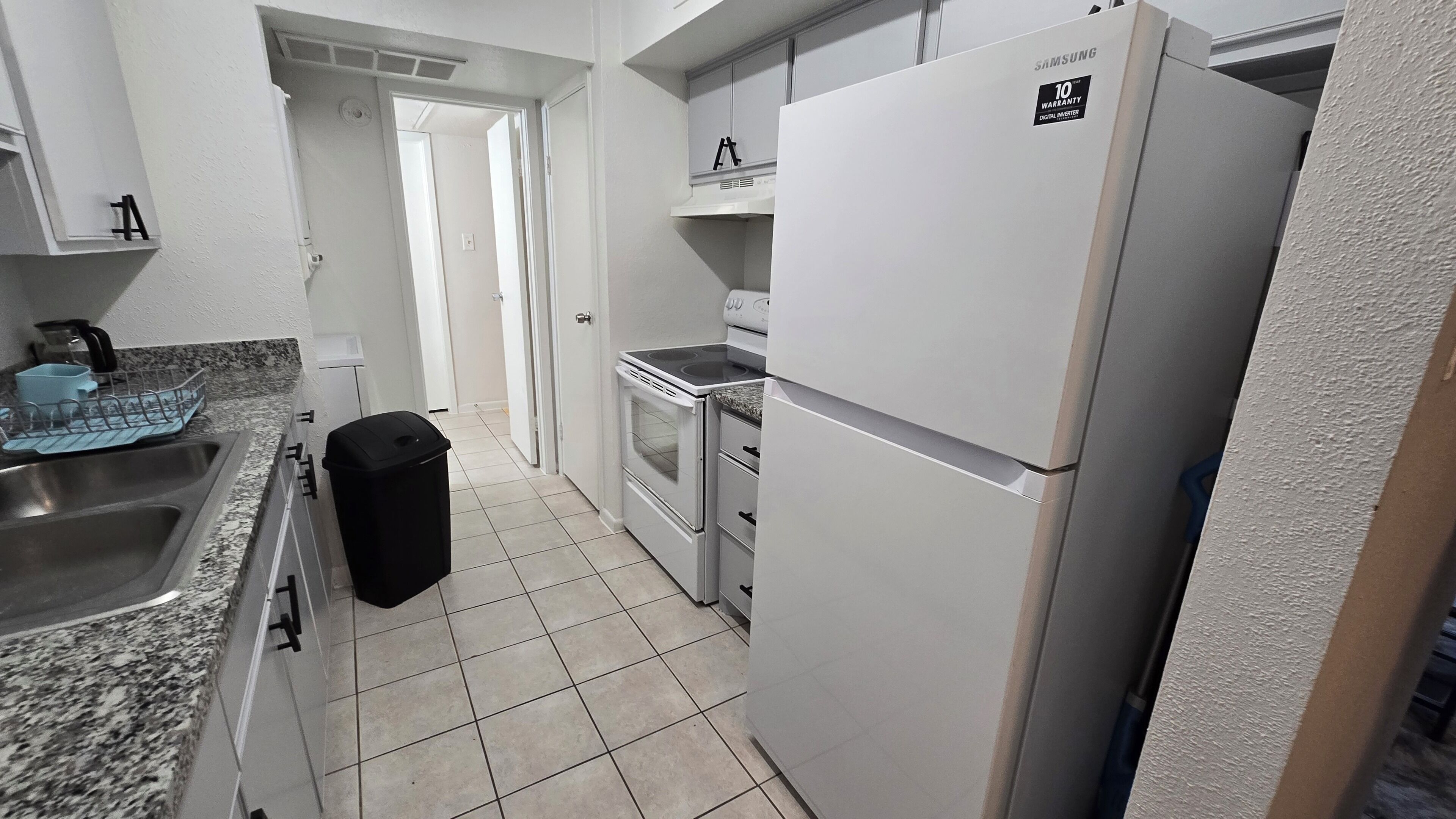 A compact kitchen with a stainless steel sink, a black trash bin, a white refrigerator, and a stove.