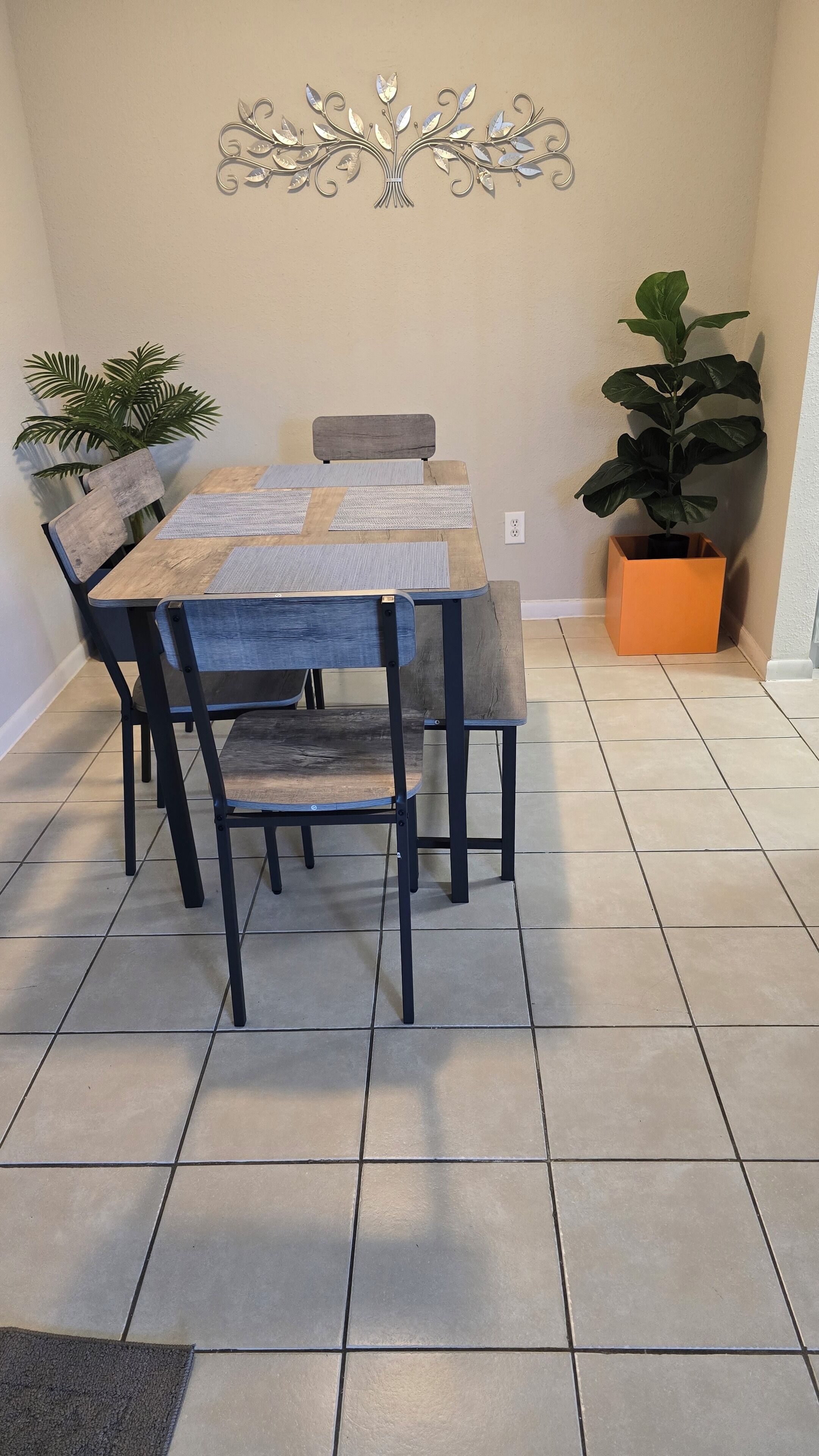 Un coin repas comprenant une table en bois, quatre chaises, un élément décoratif mural et deux plantes en pot.