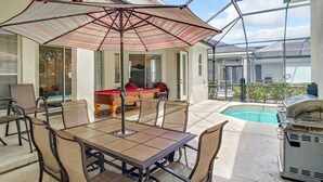 Eine sonnige Terrasse mit Billardtisch, Stühlen und Grill.