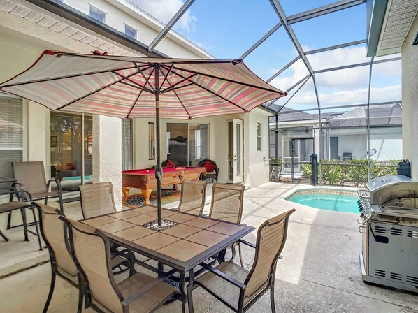 Une terrasse ensoleillée avec une table de billard, des chaises et un barbecue.