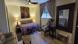 A hotel room with a bed, two bedside tables, a desk, a chair, a sofa, a small table, a mirror, and a ceiling fan.