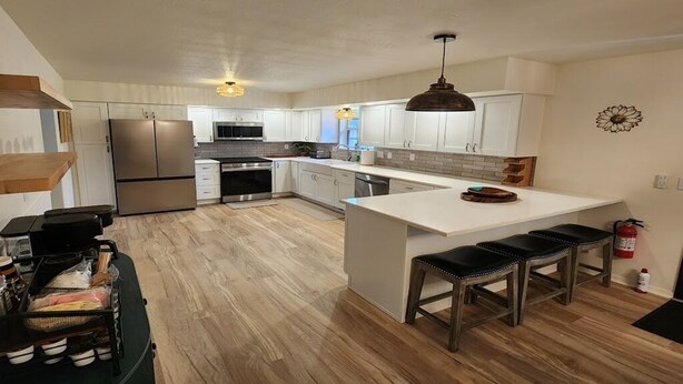 A modern kitchen with white cabinets, stainless steel appliances, a central island with stools, and a hanging pendant light.