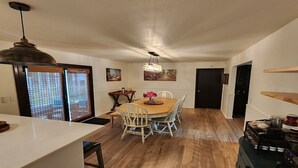 A dining area with a wooden table, white chairs, a chandelier, and a kitchen area with a stove.