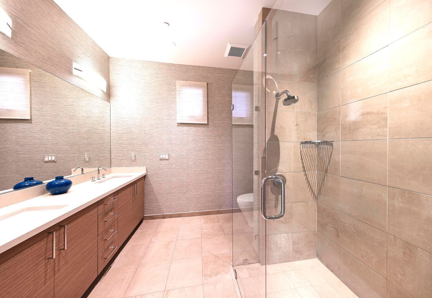 A modern bathroom with a glass shower enclosure, a large mirror, and a wooden vanity with two blue vases.