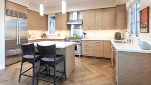 Une cuisine moderne dotée d’un îlot central, d’appareils électroménagers en acier inoxydable et de meubles de rangement en bois.