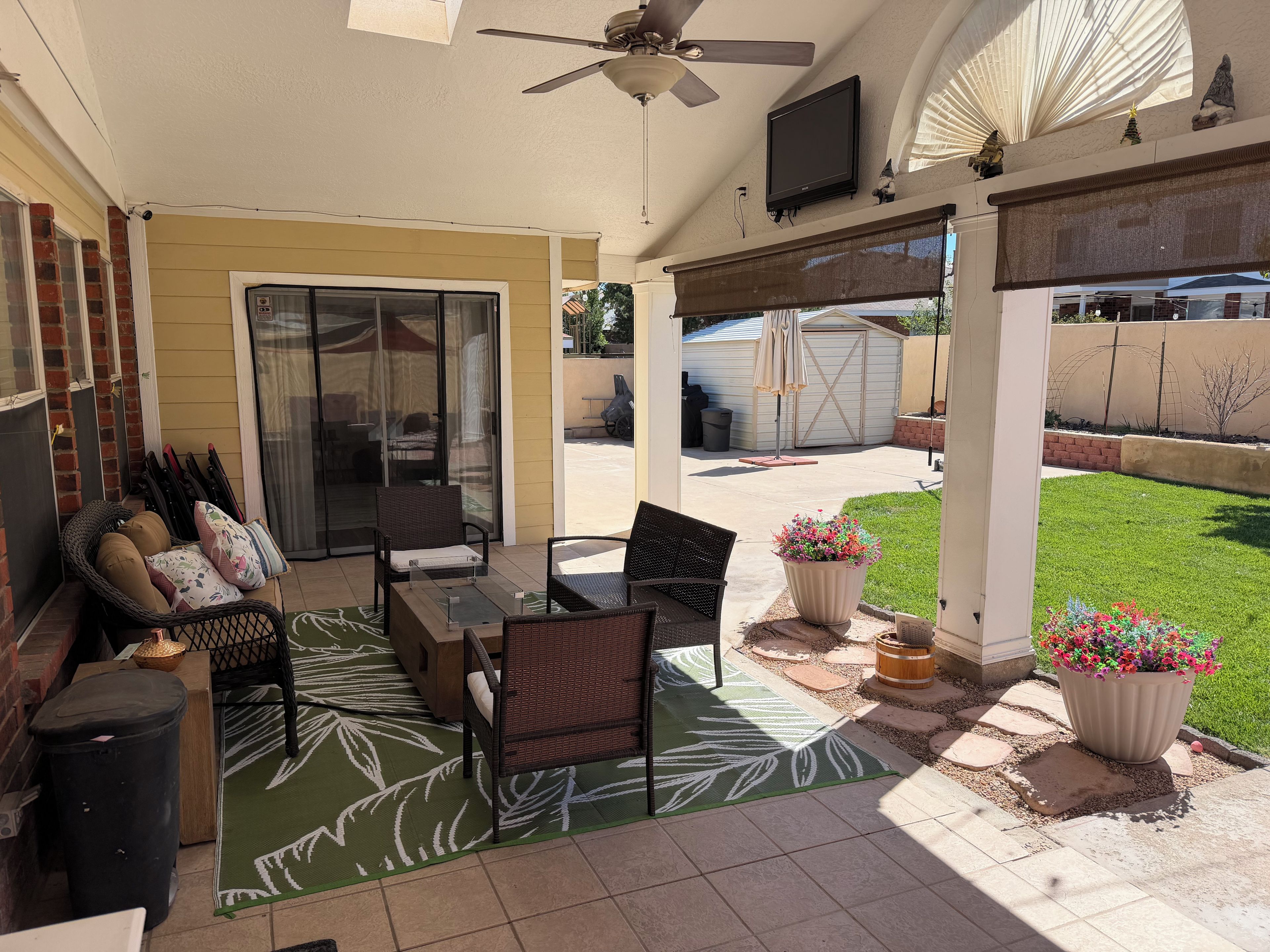 A covered patio area with a ceiling fan, outdoor seating, and a TV mounted on the wall.