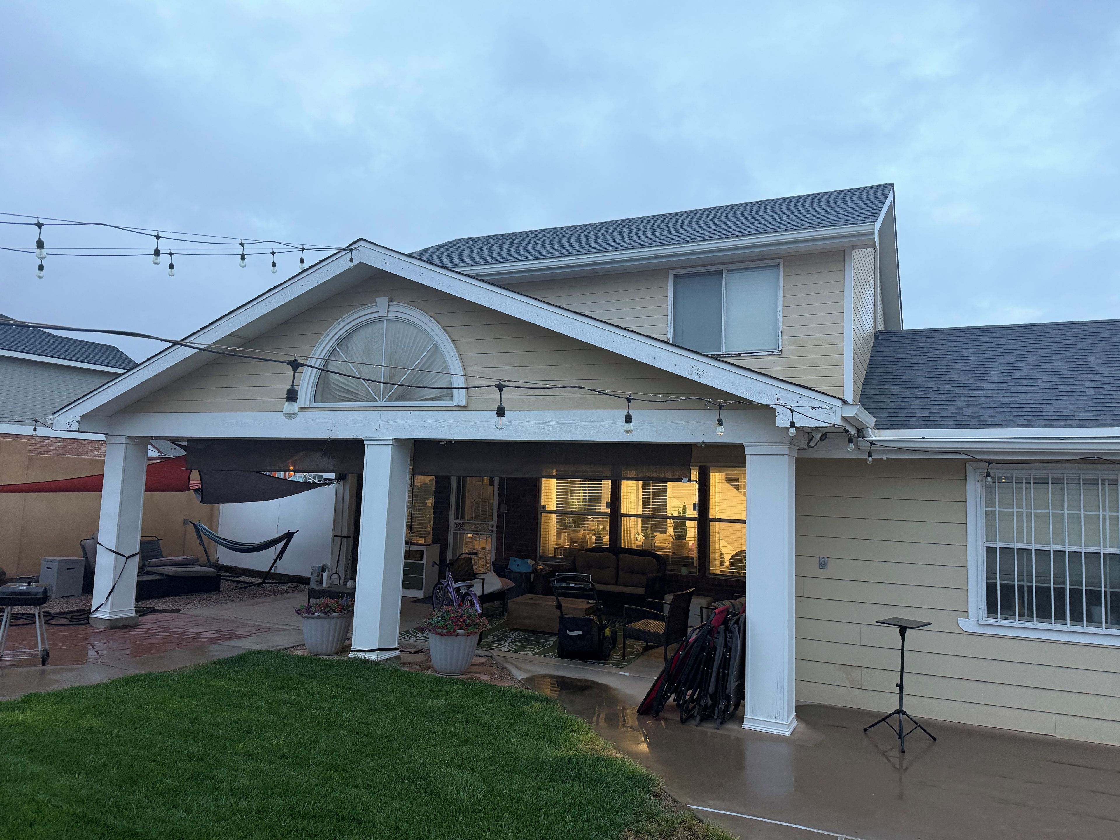 A two-story house with a covered patio, outdoor furniture, and string lights.