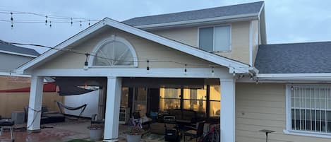 A two-story house with a covered patio, outdoor furniture, and string lights.