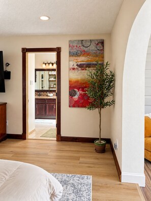 Un interior moderno con piso de madera, un cuadro abstracto grande y una planta en maceta.