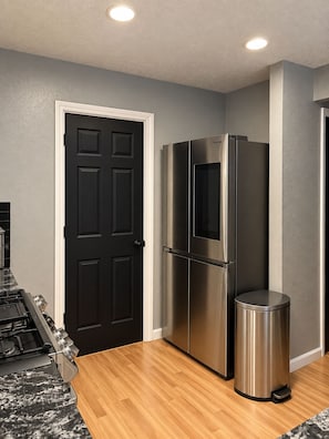A kitchen with a stainless steel refrigerator, a trash can, and a black door. - ABQ Getaway Kings, 3 Bdrm, 2.5 Bath, Patio Large Yard, Primary Suite & Game Loft (Albuquerque)
