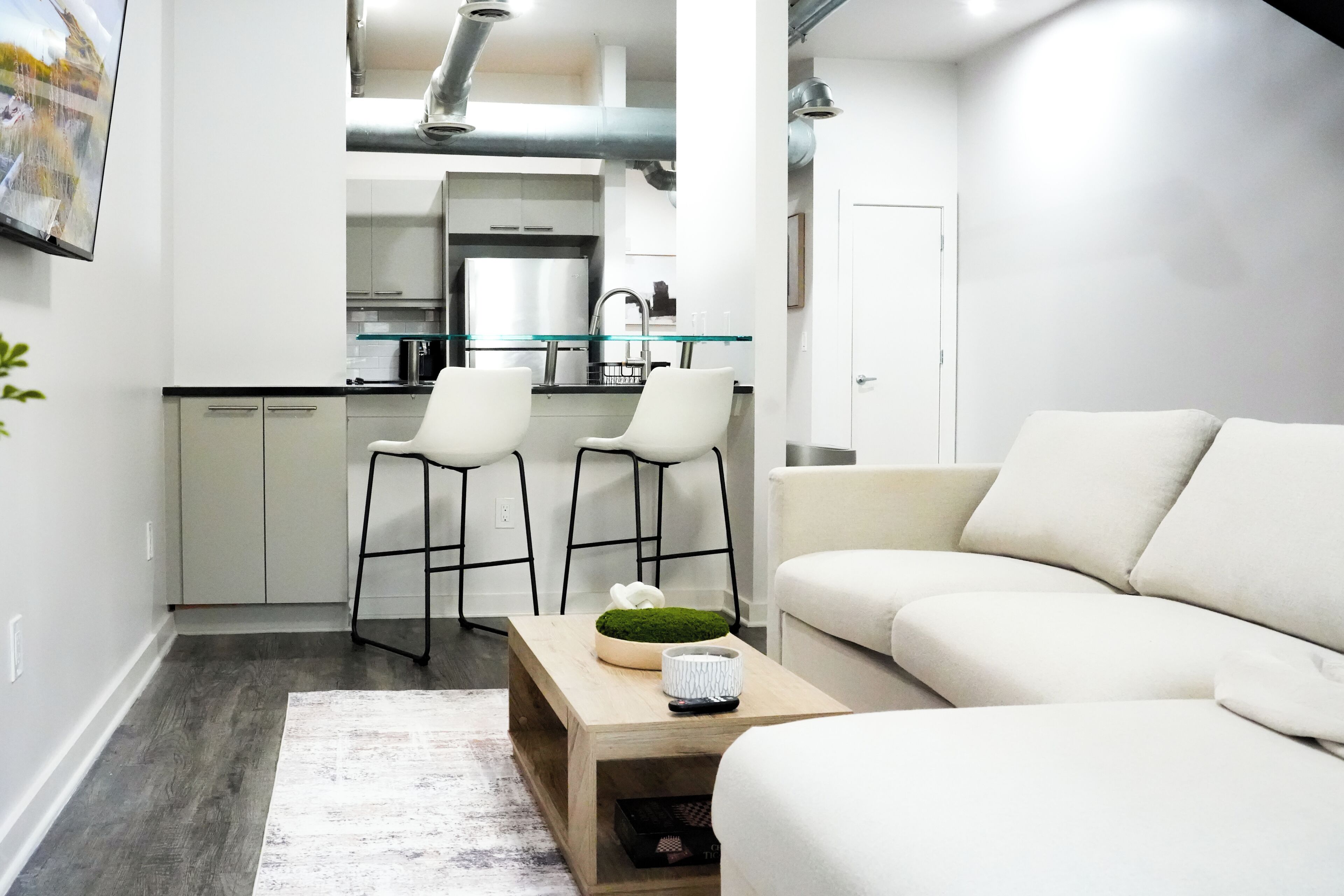 Una sala de estar moderna con un sofá, una mesa de centro con objetos decorativos y una cocina al fondo.