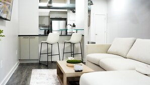 Ein modernes Wohnzimmer mit einer Couch, einem Couchtisch mit Dekoration und einer Küche im Hintergrund.