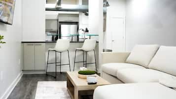 Una sala de estar moderna con un sofá, una mesa de centro con objetos decorativos y una cocina al fondo.