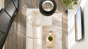 Ein modernes Wohnzimmer mit einem weißen Sofa, einem Holztisch mit einer grünen Schüssel und einer Pendelleuchte.