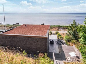A modern building with a flat roof, a patio area with outdoor seating, and a view of the sea.