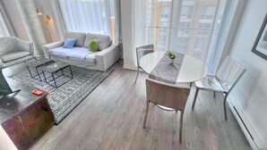 Uma sala de estar moderna com um sofá, uma mesa de centro, uma mesa de jantar com cadeiras e janelas amplas com cortinas.