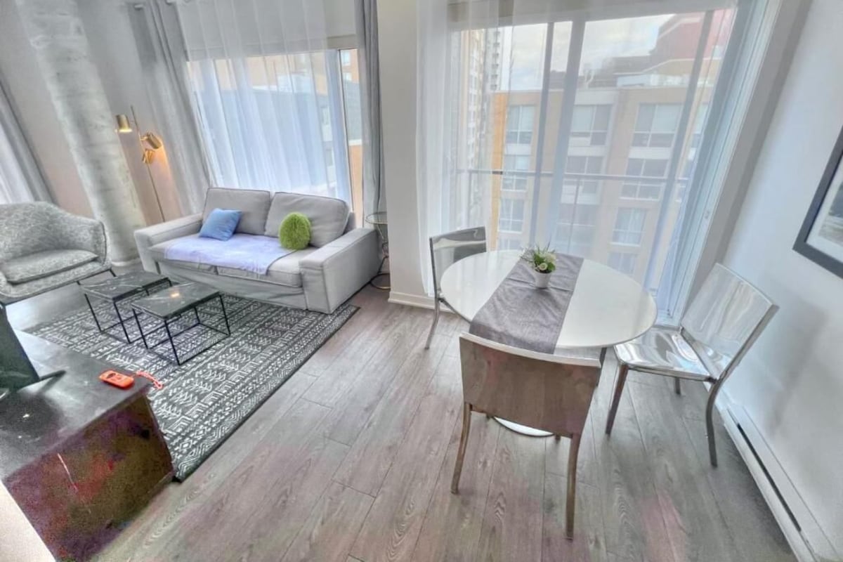 Una sala de estar moderna con un sofá, una mesa de centro, una mesa de comedor con sillas y ventanas amplias con cortinas.