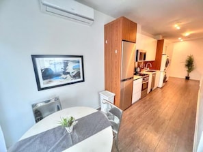 Una cocina moderna con armarios de madera, un refrigerador y un lavamanos. Hay una zona de comedor con una mesa y sillas.