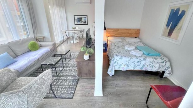 Visão dividida de um quarto com sofá, mesa pequena, cama e cadeira.