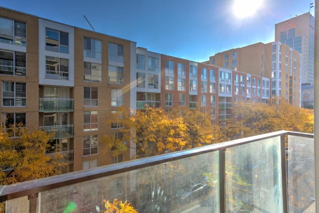 Ein mehrgeschossiges Gebäude mit einem Glasbalkon, umgeben von Herbstbäumen.