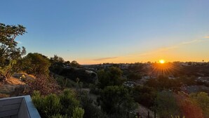 Zonsondergang vanaf een balkon met uitzicht op een woongebied met bomen en een heldere lucht.