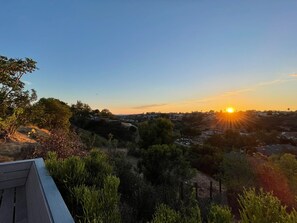 Sonnenuntergangblick von einem Balkon mit Blick auf eine Wohngegend, Bäume und einen klaren Himmel.