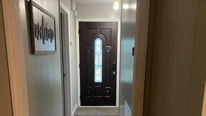 A hallway with a dark wooden door, a welcome sign, and a light fixture. - Luxury Stay Gastonia (Gastonia)