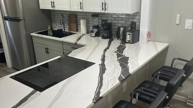A modern kitchen with white cabinets, a black countertop, and a built-in island with bar stools. - Luxury Stay Gastonia (Gastonia)