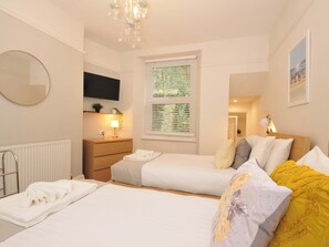 Habitación de hotel con cama, mesita de noche, espejo, televisión, ventana con persianas y candelabro.