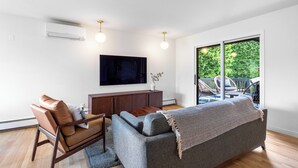 A modern living room with a sofa, a television, and a view of the outdoors. - Seattle Mid-century Reteat (Burien)