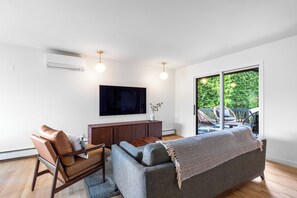 Ein modernes Wohnzimmer mit einer Couch, einem Fernseher und Blick ins Freie.