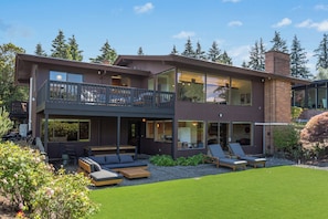 Ein modernes, zweistöckiges Haus mit Balkon, Sitzgelegenheit im Freien und einem gepflegten Rasen.