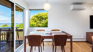 A dining area with a table, chairs, a hanging light fixture, and a large window with a view of greenery. - Seattle Mid-century Reteat (Burien)