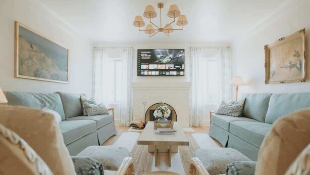 A living room with two sofas, a coffee table, a TV mounted on the wall, and a chandelier. - French Tea House in Old Town+Private Hot Tub+Pet Friendly! (Albuquerque)