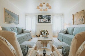 Ett vardagsrum med två soffor, ett soffbord, en tv som är monterad på väggen och en kristallkrona.