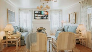 A living room with two sofas, a coffee table, and lamps. There is a television mounted on the wall. - French Tea House in Old Town+Private Hot Tub+Pet Friendly! (Albuquerque)