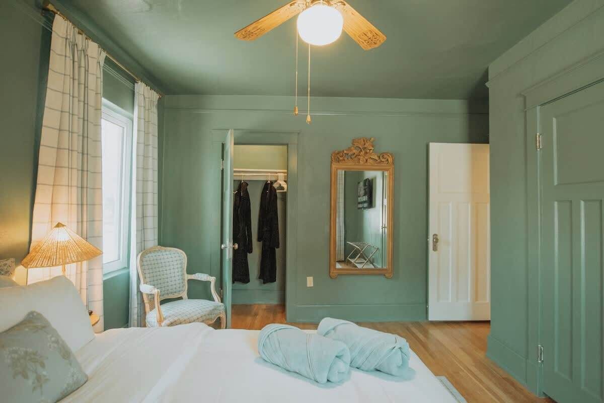 A bedroom with a bed, a chair, a mirror, and a wardrobe.