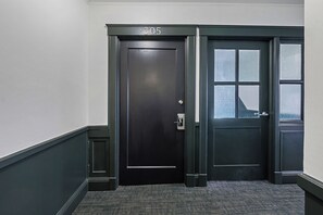 Eine dunkel gefärbte Tür mit der Nummer 305, ein kleines Fenster und ein strukturierter Teppichboden.