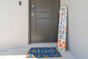 A door with a 'WELCOME' sign, a 'HELLO' mat, and a doorbell. - Lehigh Fun Home (Lehigh Acres)
