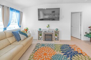A living room with a sofa, a fireplace, a TV, and a patterned rug. - Lehigh Fun Home (Lehigh Acres)
