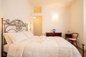 A neatly made bed with a metal headboard, a bedside table with a vase, and a chair. - Dimora BoxFish | Elegance and Relaxation with a Private Terrace (Polignano a Mare)