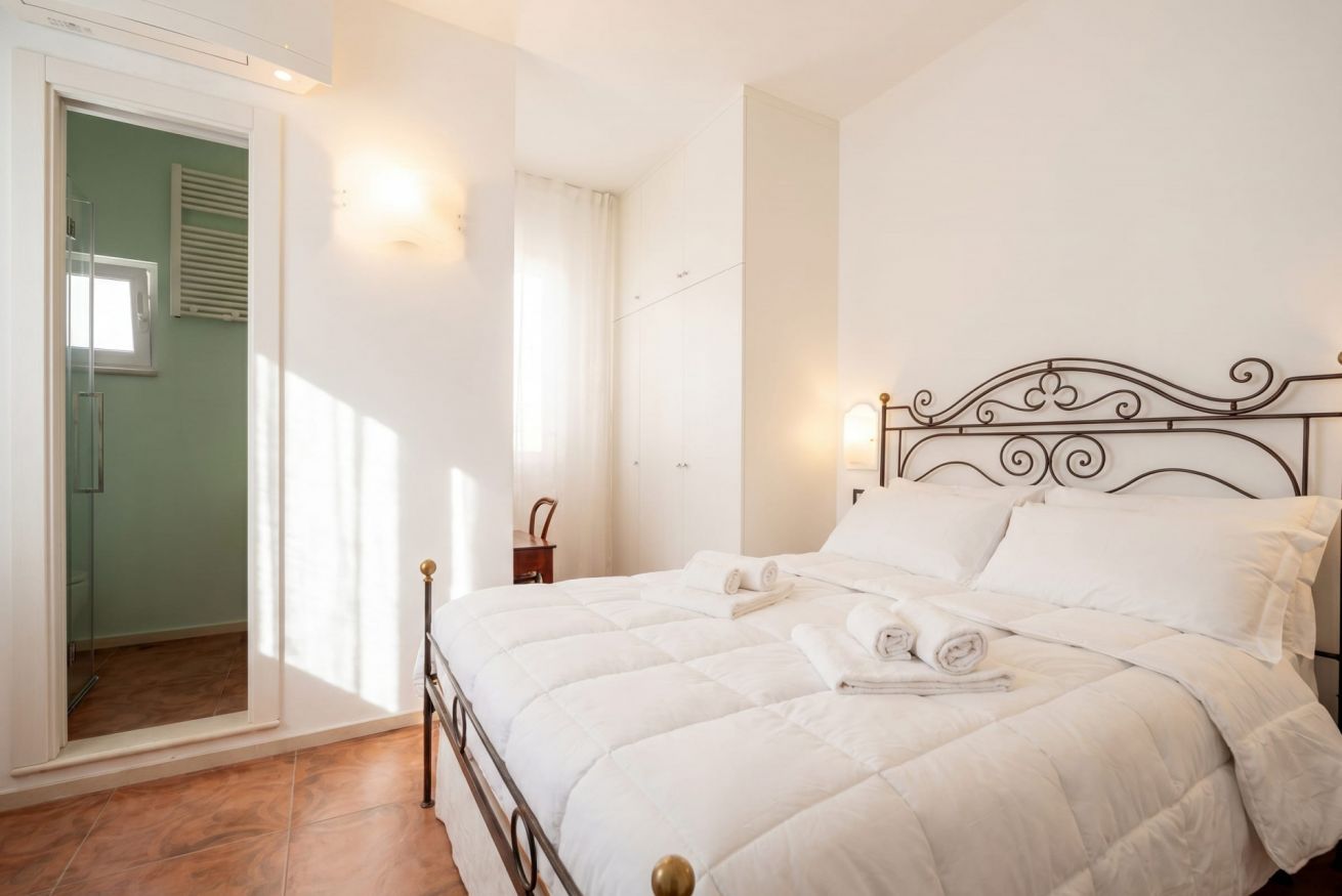 Une chambre à coucher comprenant un lit, une table de chevet, une lampe fixée au mur et une porte donnant sur une autre pièce.