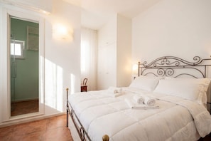 A bedroom with a bed, a nightstand, a wall-mounted light, and a door leading to another room. - Dimora BoxFish | Elegance and Relaxation with a Private Terrace (Polignano a Mare)