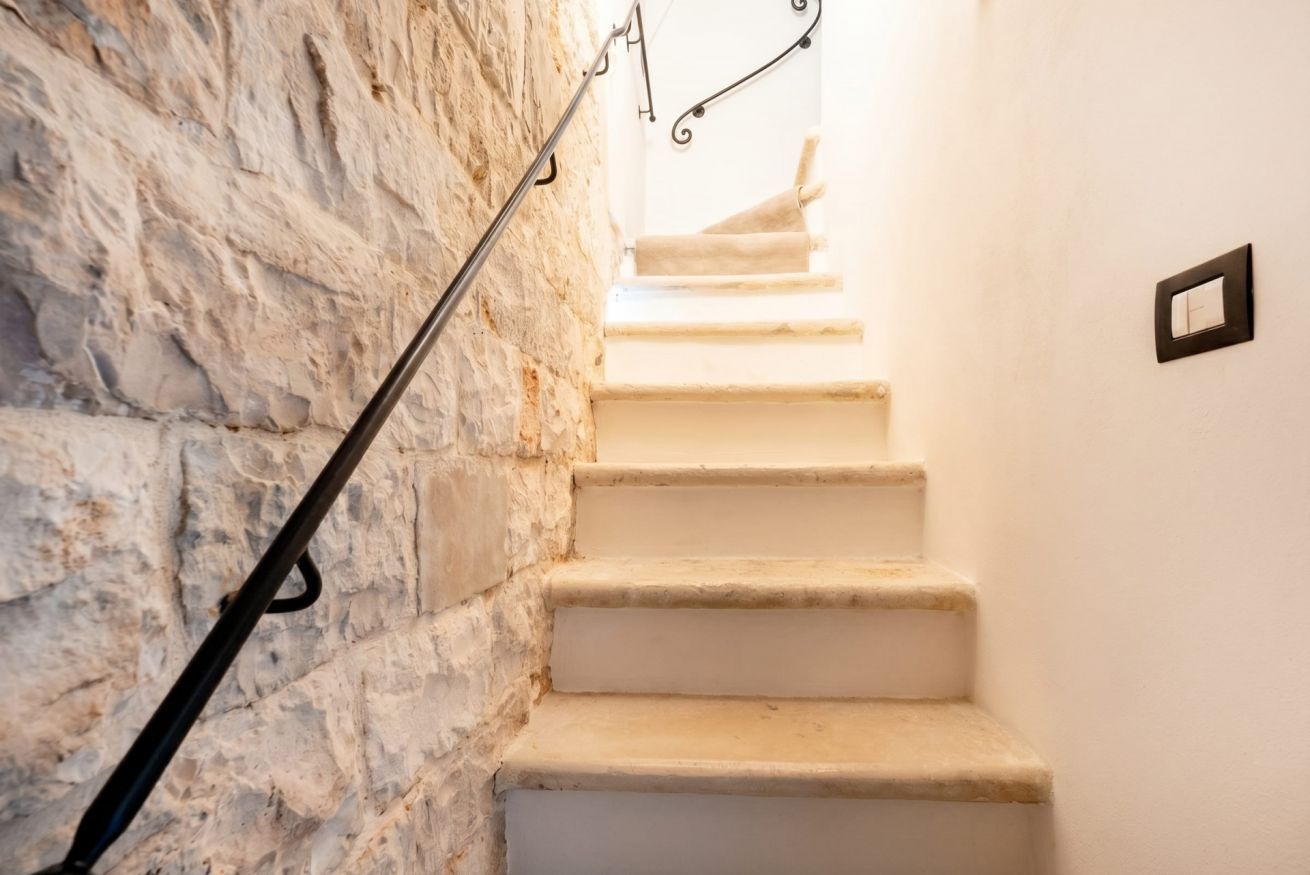 Eine Treppe mit einer Steinsäule auf einer Seite und einer weißen Wand auf der anderen, die zu einer höheren Etage führt.