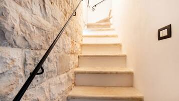 Eine Treppe mit einer Steinsäule auf einer Seite und einer weißen Wand auf der anderen, die zu einer höheren Etage führt.