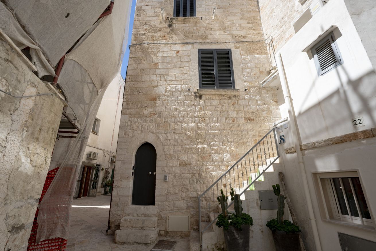 A narrow alleyway with stone buildings, a black door, and a staircase leading to an upper level.