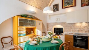 Un comedor con mantel verde, sillas de madera, un armario amarillo con puertas de vidrio, un televisor y una pared de piedra.